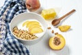 white wheat granola with low-fat yogurt in a white bowl in a composition with a spoon, honeycombs and peach on white wooden