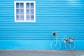 White window on the blue wall with bike shaped flowers pot.