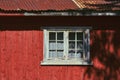 White window on a red wooden house with a rusty rooftop.