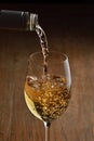 White wine Being Poured into Glass. Stream of wine from bottle and swirls and bubbles in glass. Glass with golden liquid.