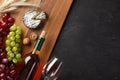 White wine bottle, bunch of grapes, cheese, ears of wheat and wineglass on wooden board and black background