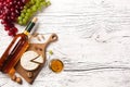 White wine bottle, grape, cheese and wineglass on white wooden board