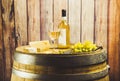 White wine in glass, bottle, grape and cheese on barrel front wood background.