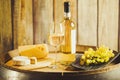 White wine in glass, bottle with grape and cheese on barrel front wood wall background.