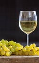 White wine in wineglass next to a bunch of grapes on a wooden table. Vertical portrait of alcohol drink and fruit on black Royalty Free Stock Photo