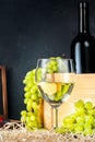 White wineglass and white yellow green bunches of berry grapes with bottle of wine