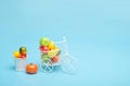 White wire bicycle with a basket filled with mini fruit. Near the bucket with vegetables and fruits. Blue background