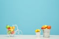 White wire bicycle with a basket filled with mini fruit. Near the bucket with vegetables and fruits. Blue background