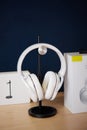 White wireless head large headphones stand on a wooden table on a black stand on a blue background side view