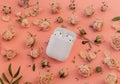 White wireless headphones in the case on playful pink background with delicate dry roses flowers