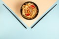 White wok noodles in black plate with black chopsticks on peach and blue background