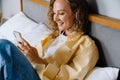 White woman using cellphone with earphones lying in bed at home Royalty Free Stock Photo