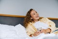 White woman using cellphone with earphones lying in bed at home Royalty Free Stock Photo