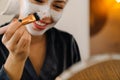 White woman wrapped towel applying face mask while looking in mirror Royalty Free Stock Photo