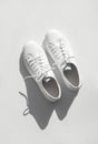 White women's leather sneakers with sun shadows on white background top view. Stylish youth sneakers, sports shoes Royalty Free Stock Photo