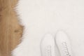 White women sneakers on white fur carpet, wooden background. Flat lay of modern white shoes. Overhead top view photography. Fitnes