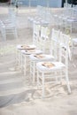 A group of white chiavari chairs on the beach wedding preparation, cones of roses petals - front side view