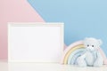 White blank frame with teddy bear and pastel toy rainbow on white desk with pink and blue background Royalty Free Stock Photo