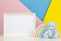 White blank wood frame with teddy bear and pastel toy rainbow on white desk and pink, yellow and blue background Royalty Free Stock Photo