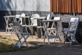 White wood tables and chairs stand without visitors on a sunny summer day near a gray stone wall. Royalty Free Stock Photo