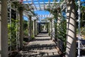 White wooden awning in the garden covered with lush green plants or colorful flowers with stone pillars and people walking