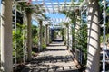 White wooden awning in the garden covered with lush green plants or colorful flowers with stone pillars and people walking