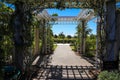 A white wooden awning in the garden covered with lush green plants and colorful flowers with a walk way leading to white flowers