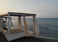 White wooden beach house sunshade parasol mattress with white curtains with a view of blue sea and waves in a romantic sunrise Royalty Free Stock Photo