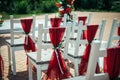 White wooden chairs decorated with red fabric and ribbons for wedding reception outdoor. Guest chairs in rows in the summer park, Royalty Free Stock Photo