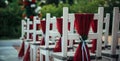 White wooden chairs decorated with red fabric and ribbons for wedding reception outdoor. Guest chairs in rows in the summer park, Royalty Free Stock Photo