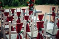 White wooden chairs decorated with red fabric and ribbons for wedding reception outdoor. Guest chairs in rows in the summer park, Royalty Free Stock Photo