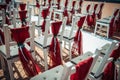 White wooden chairs decorated with red fabric and ribbons for wedding registration outdoor. Guest chairs in rows, close up Royalty Free Stock Photo