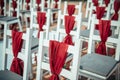 White wooden chairs decorated with red fabric and ribbons for wedding registration outdoor. Guest chairs in rows, close up Royalty Free Stock Photo