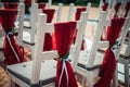 White wooden chairs decorated with red fabric and ribbons for wedding registration outdoor. Guest chairs in rows, close up Royalty Free Stock Photo