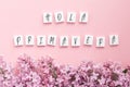 wooden cubes with the inscription hello spring in Spanish, Italian and Portuguese lilac branches on a pink background