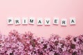 white wooden cubes with the inscription spring in Spanish, Italian and Portuguese lilac branches on a pink background