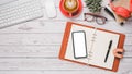 White wooden desk workplace with blank screen smartphone, notebook, pen, keyboard, mouse, eyeglass, headphone, notebook and cup of Royalty Free Stock Photo