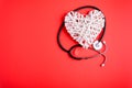 White wooden heart with black stethoscope on red paper background. Heart health concept.