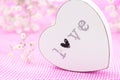 White wooden heart closeup with word Love, on pink mesh fabric and white flowers