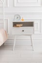 White wooden nightstand with alarm clock and books. Scandinavian style white interior