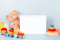 White wooden picture frame with blank mock up copy space standing next to teddy bear and colorful wooden toy train and Royalty Free Stock Photo