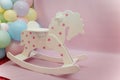 White wooden rocking horse with  stars and colorful balloons on pink background. Little girl room interior or first birthday party Royalty Free Stock Photo