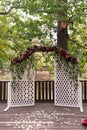 White wooden rustic arch for the wedding ceremony, decorated with red flowers and greenery