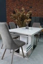 White wooden table combined with gray wooden chairs with soft fabric upholstery. There is a black glass vase with dried Royalty Free Stock Photo