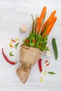 On a white wooden table lies a vegetarian bouquet consisting of carrots, pea pods, salad, pepper and aloe. Nearby is garlic, red d