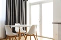 White wooden table and three plastic chairs are standing next to the big white window. Black curtain on the backround Royalty Free Stock Photo