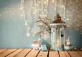 White wooden vintage lantern with burning candle, wooden deer, christmas gifts and tree branches on wooden table. retro filtered i