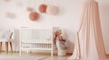 White woolen blanket and pastel pink pompom placed on a wooden crib with canopy in bright baby room interior with poster on the Royalty Free Stock Photo