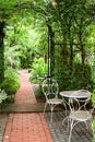 White wrought iron table and chairs in the garden with bricks paved walkway Royalty Free Stock Photo