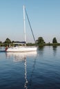 A white yacht with lowered sails and Lithuania flag in the lagoon. Quiet evening, well visible reflection of the ship`s mast in